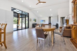A spacious living area with a large round table, comfortable seating, a fireplace, and a view through a glass door to the outdoors. - Secluded Stay: Ideal for those seeking a quiet break close to nature (Toorloo Arm)