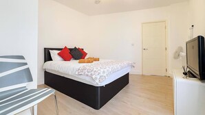 A bedroom with a bed, a chair, a TV, and a door. - Charming High Wycombe Apartment (High Wycombe)