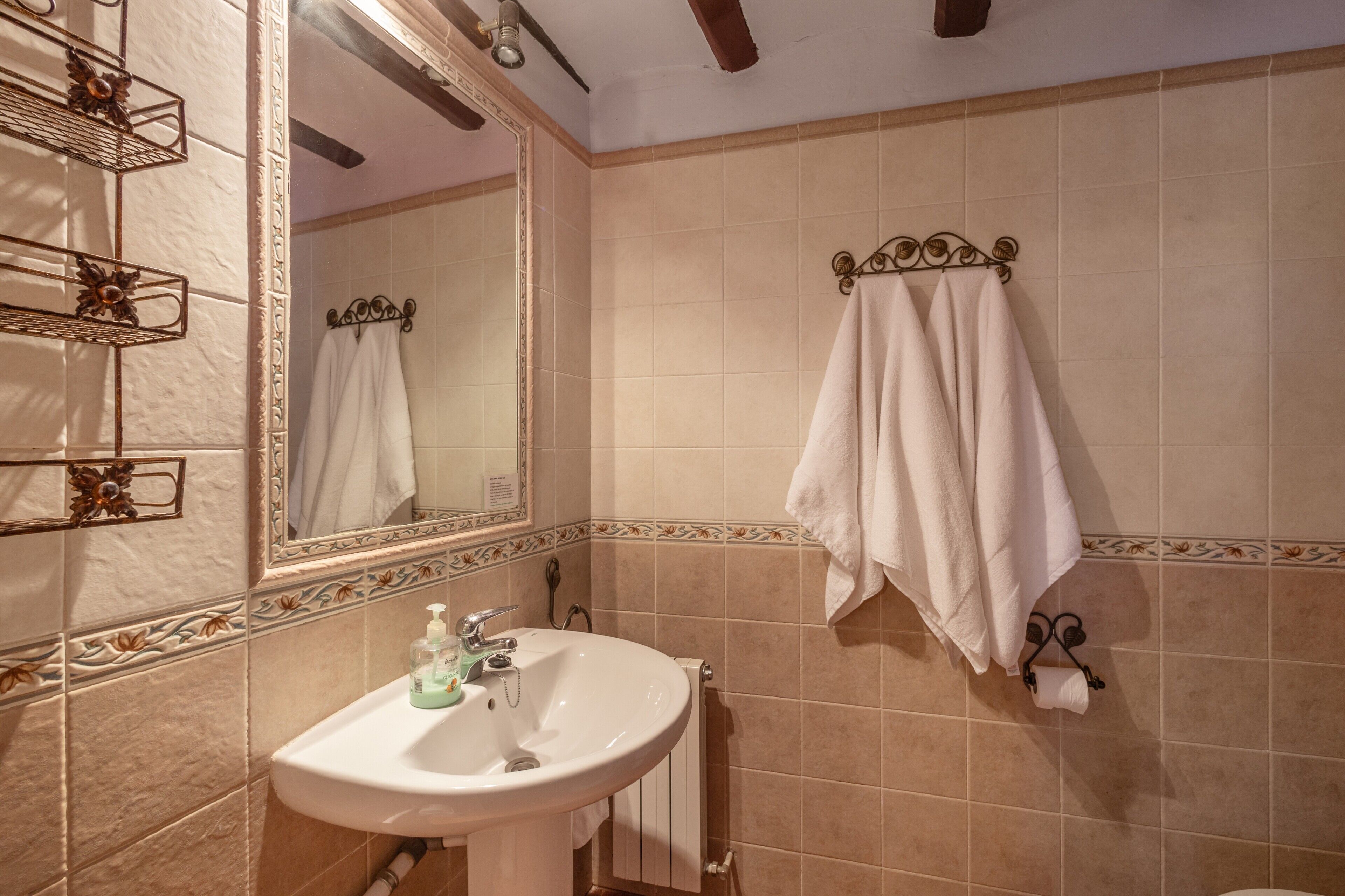Un baño con lavamanos, espejo, toallero y azulejos decorativos.