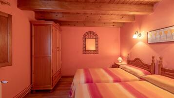 Quarto com duas camas, guarda-roupa de madeira, espelho com moldura decorativa e uma luminária fixada na parede.