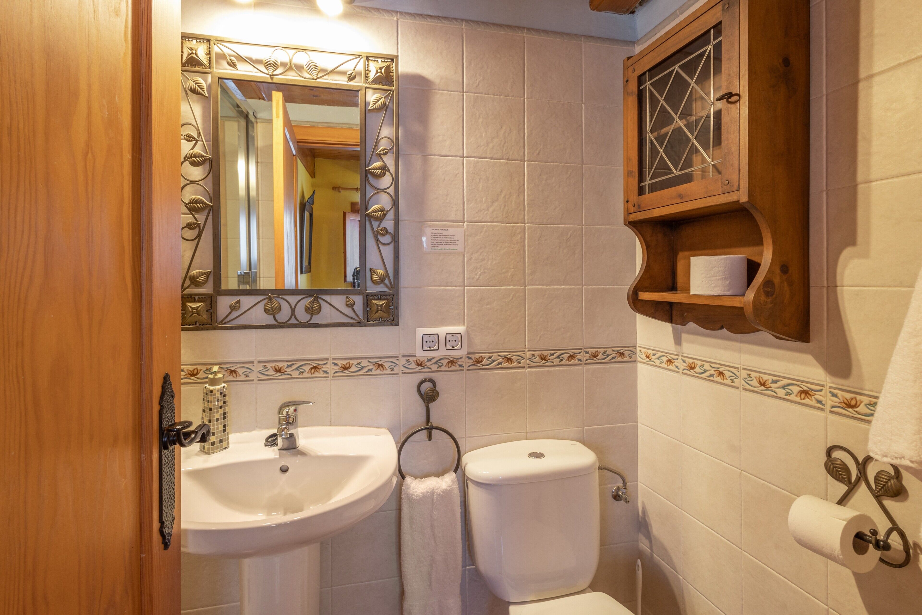 Een badkamer met een wastafel, toilet en spiegel met decoratieve bladeren.