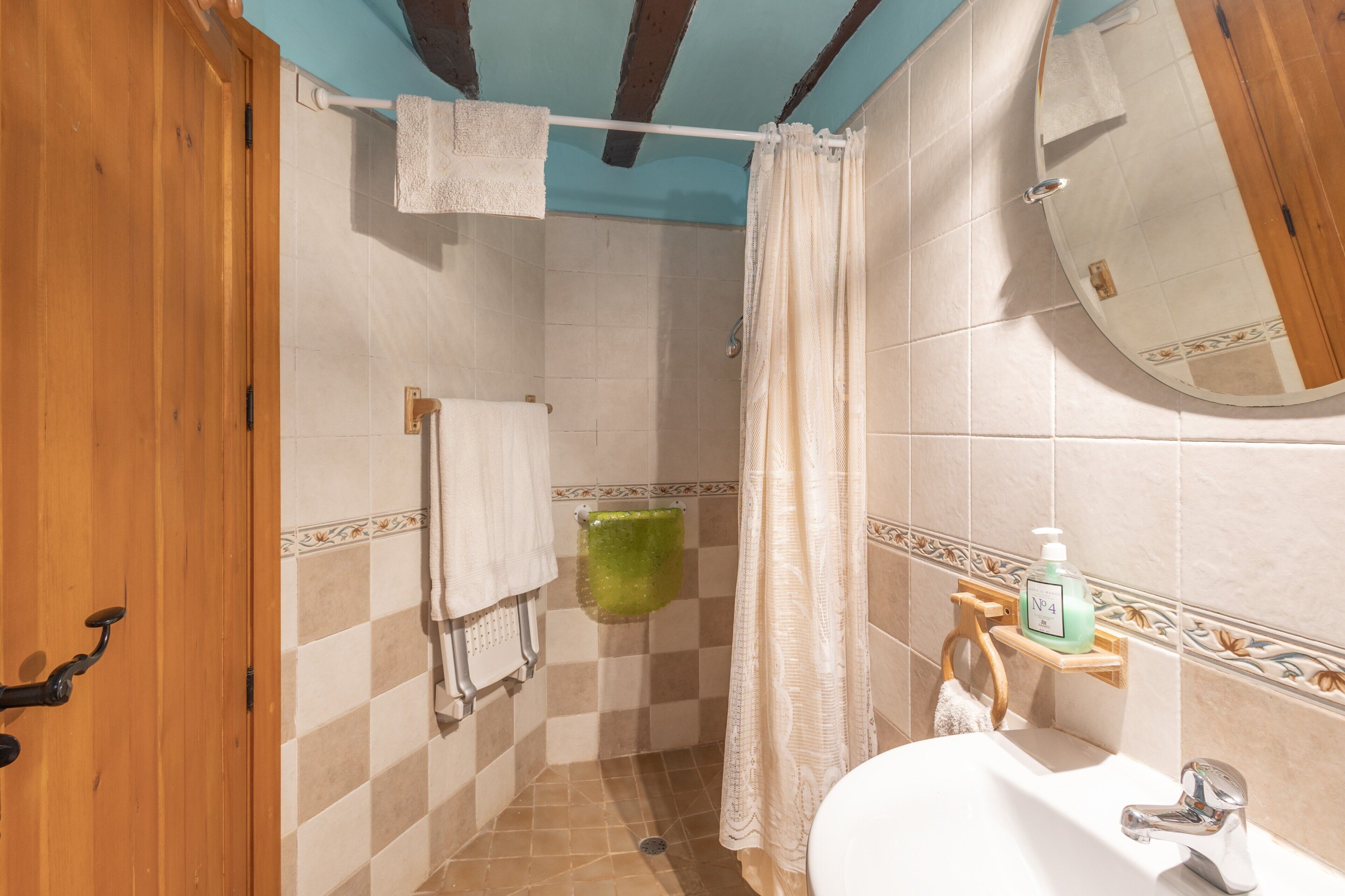 Een badkamer met een douche, wastafel, spiegel en handdoekhouder.