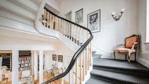 A grand staircase with a black handrail, leading to a landing with a chair and a bookshelf. - Villa Hedwig - Schwarzwald (Badenweiler)