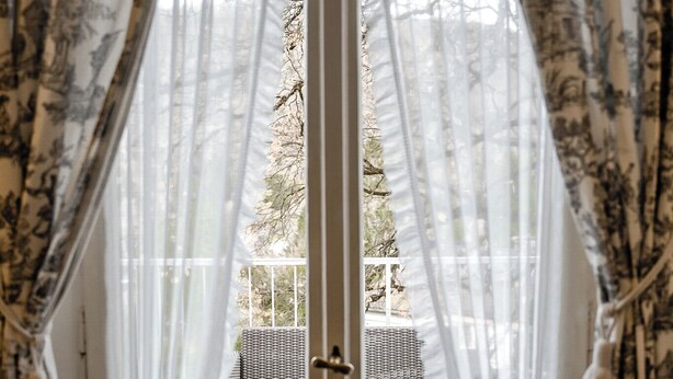 A room with a view through a window with sheer curtains, wicker furniture, and a door. - Villa Hedwig - Schwarzwald (Badenweiler)