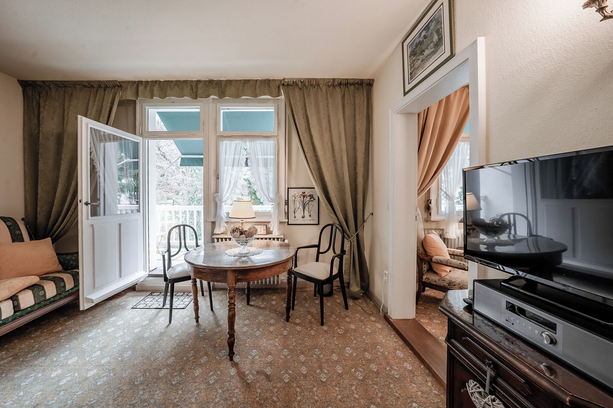 Ein gemütliches Wohnzimmer mit einer Couch, einem Esstisch mit Stühlen, einem Fernseher und einem Fenster mit Vorhängen.