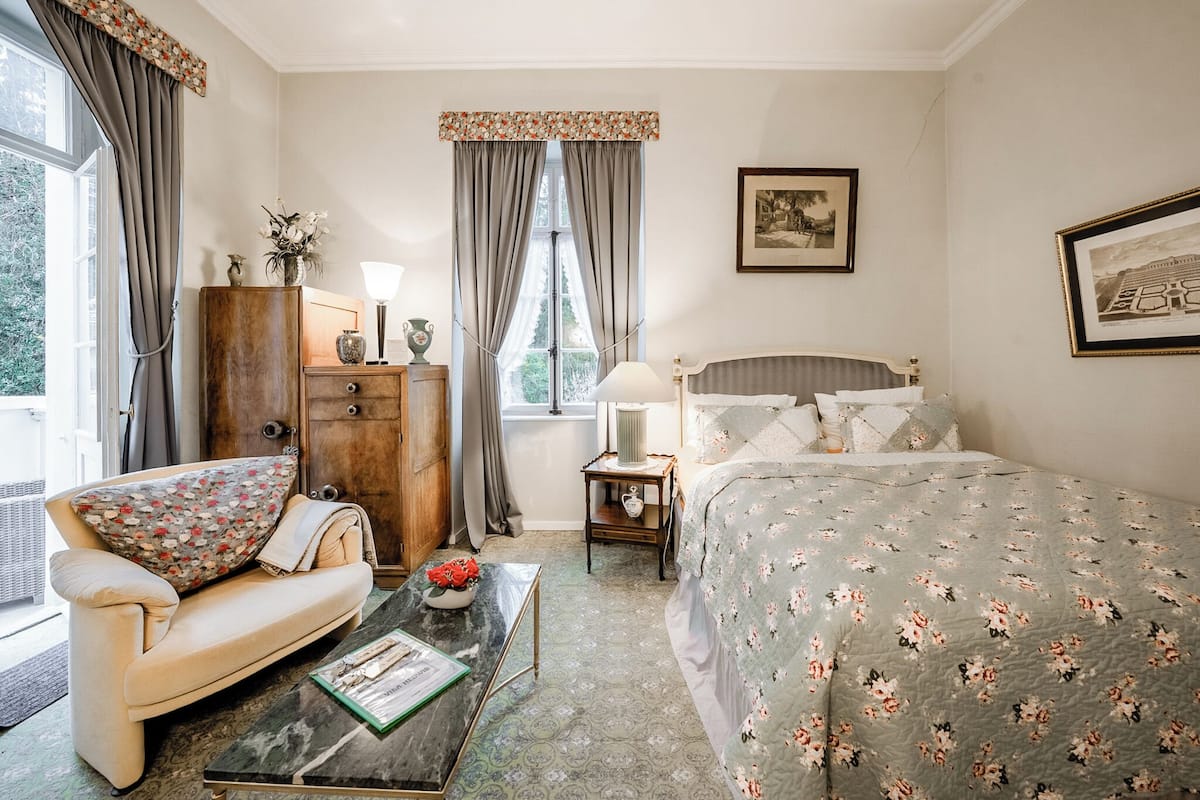 A bedroom with a bed, a sofa, a wooden cabinet, a side table, and a window with curtains.