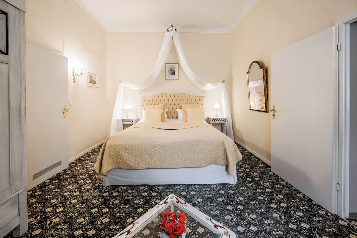 A bedroom with a large bed, two bedside tables, a canopy bed, a mirror, and a patterned carpet.