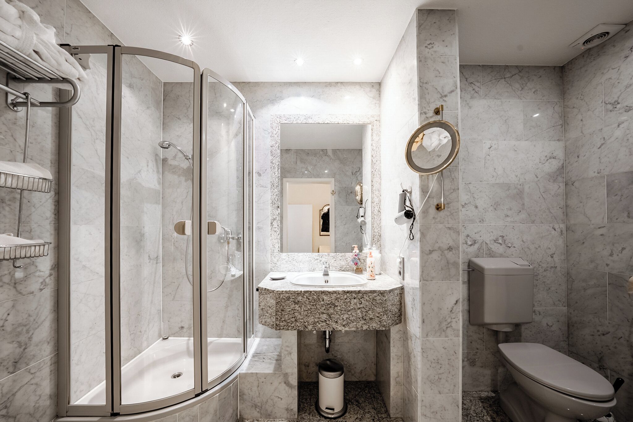 Un baño moderno con ducha de vidrio, lavamanos de mármol y un inodoro.