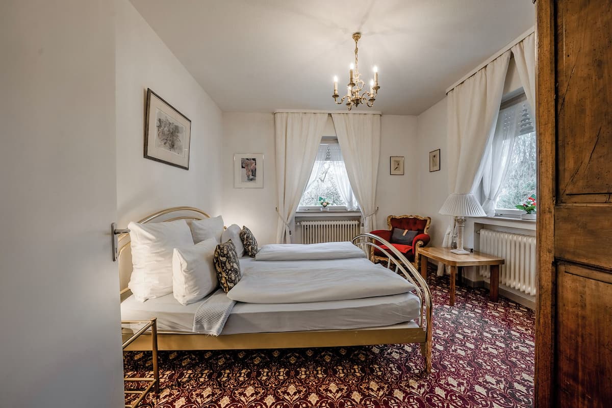 A bedroom with a bed, a chair, a table, and a window with curtains.