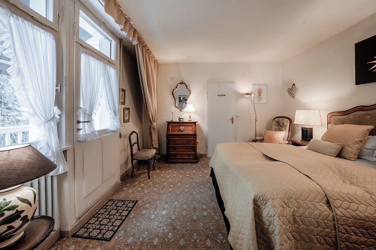 A bedroom with a bed, a dresser, a chair, a desk, and a window with curtains.