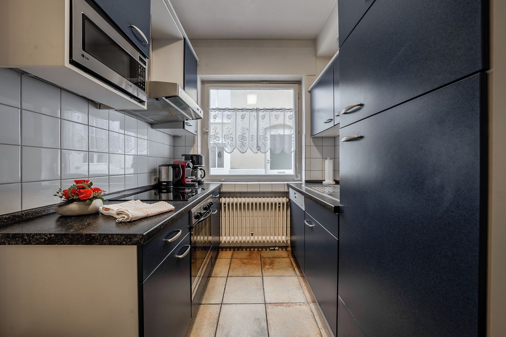 A compact kitchen with dark cabinets, a microwave, and a window with a decorative curtain.