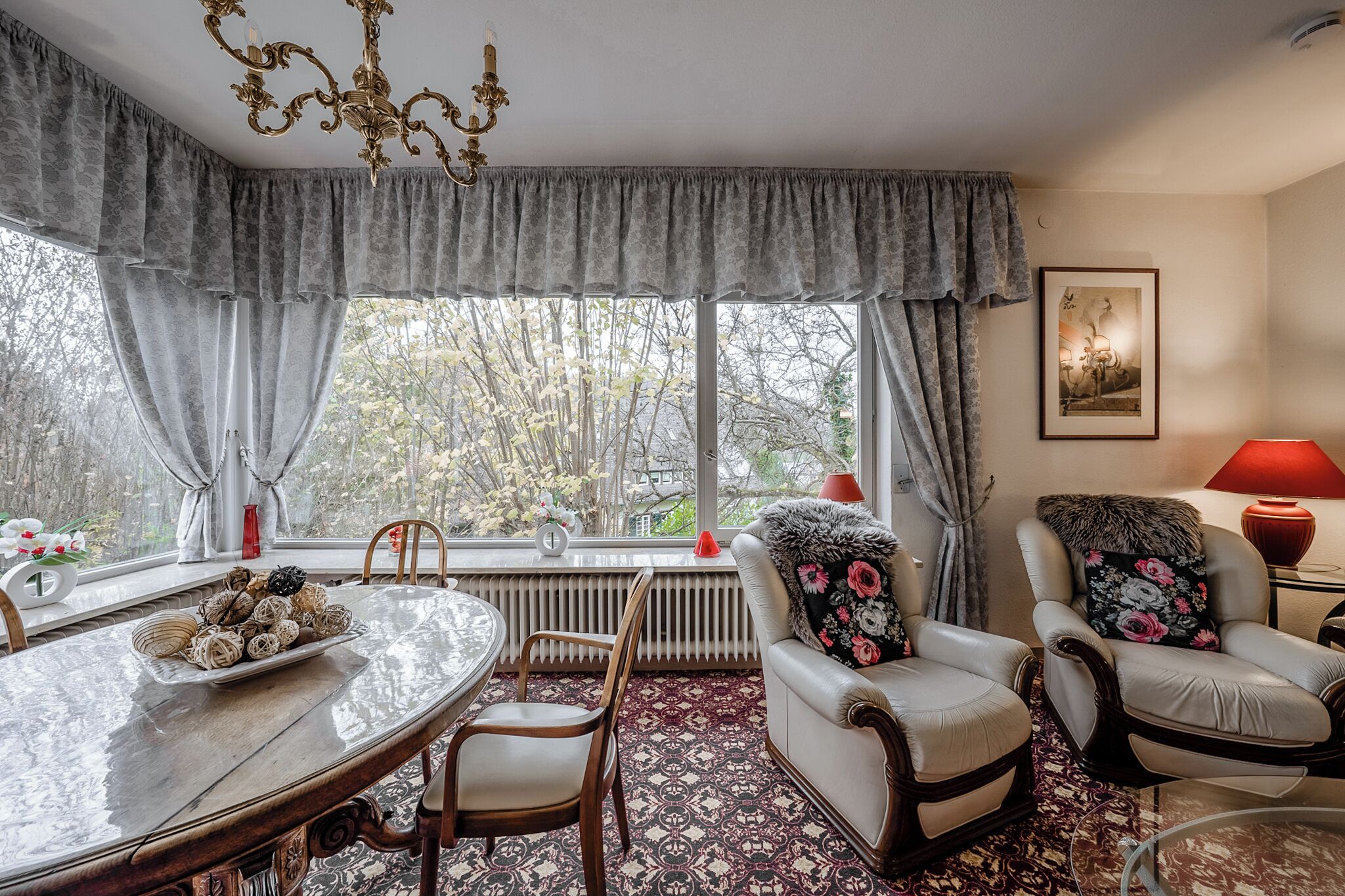 A room with a dining table, two chairs, a radiator, and a window with curtains.