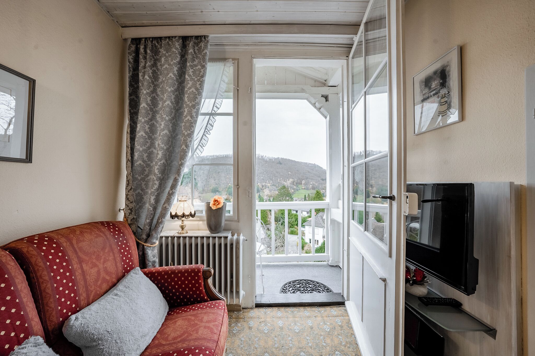 A cozy living room with a red sofa, a television, and a view of a balcony with a door leading outside.