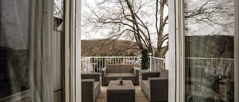 A patio area with wicker furniture and a view of a tree-lined hill.