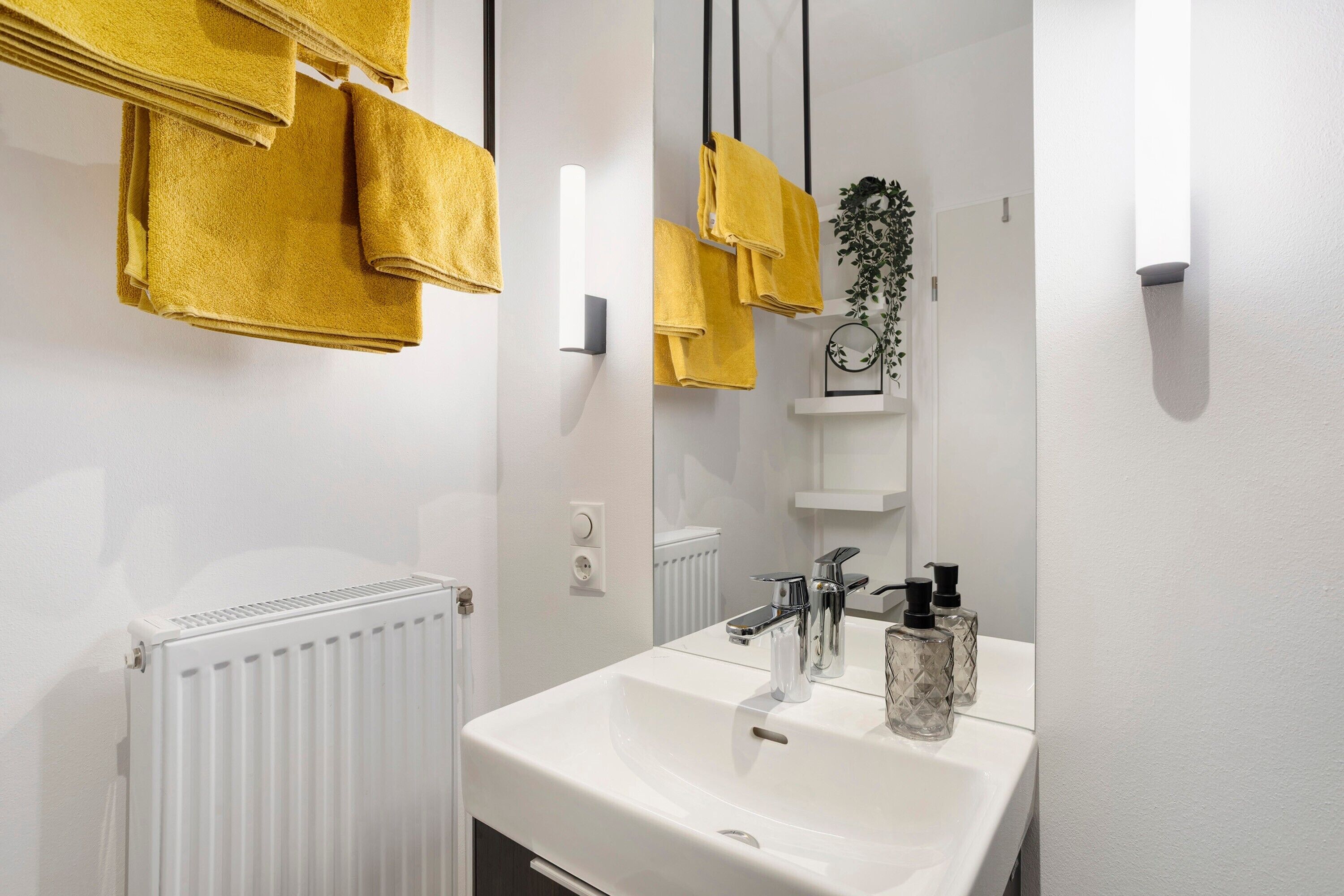 Une salle de bain avec un lavabo blanc, un miroir et des serviettes jaunes suspendues à un porte-serviettes.