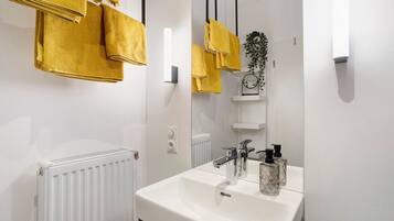 Une salle de bain avec un lavabo blanc, un miroir et des serviettes jaunes suspendues à un porte-serviettes.