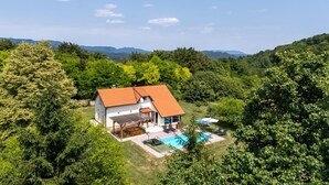 Una casa dal tetto rosso, circondata da un lussureggiante verde e una piscina.