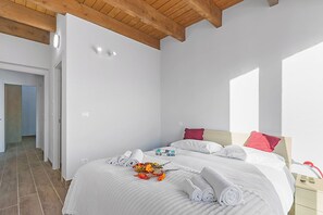 Una habitación de hotel con techo de madera, una cama con ropa blanca, una mesita de noche y una puerta que da a otra habitación.