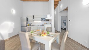 A modern kitchen with white cabinets, a stainless steel refrigerator, and a dining area with a white table and chairs. - Tana Delle Volpi Alpine Apt for 6 (Cesana Torinese)
