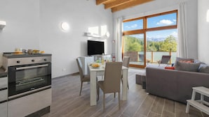 A modern kitchen with a built-in oven, a dining area with a table and chairs, a sofa, and a large window offering a mountain view. - Tana Delle Volpi Alpine Apt for 6 (Cesana Torinese)