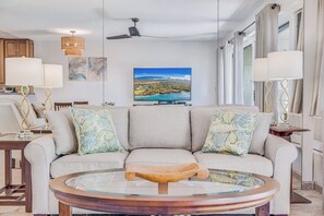 Ein modernes Wohnzimmer mit einer Couch, einem Couchtisch, einem Fernseher und Blick auf eine Küstenlandschaft.