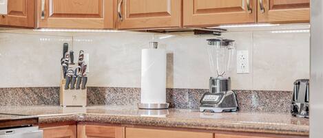 A kitchen with wooden cabinets, a granite countertop, a knife block, a paper towel holder, a blender, and a toaster.