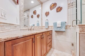 A bathroom with a wooden vanity, a large mirror, and decorative wall art. - Maui Kamaole #I-106 Ground Flr, Garden View, A/C, Great Location (Kihei)