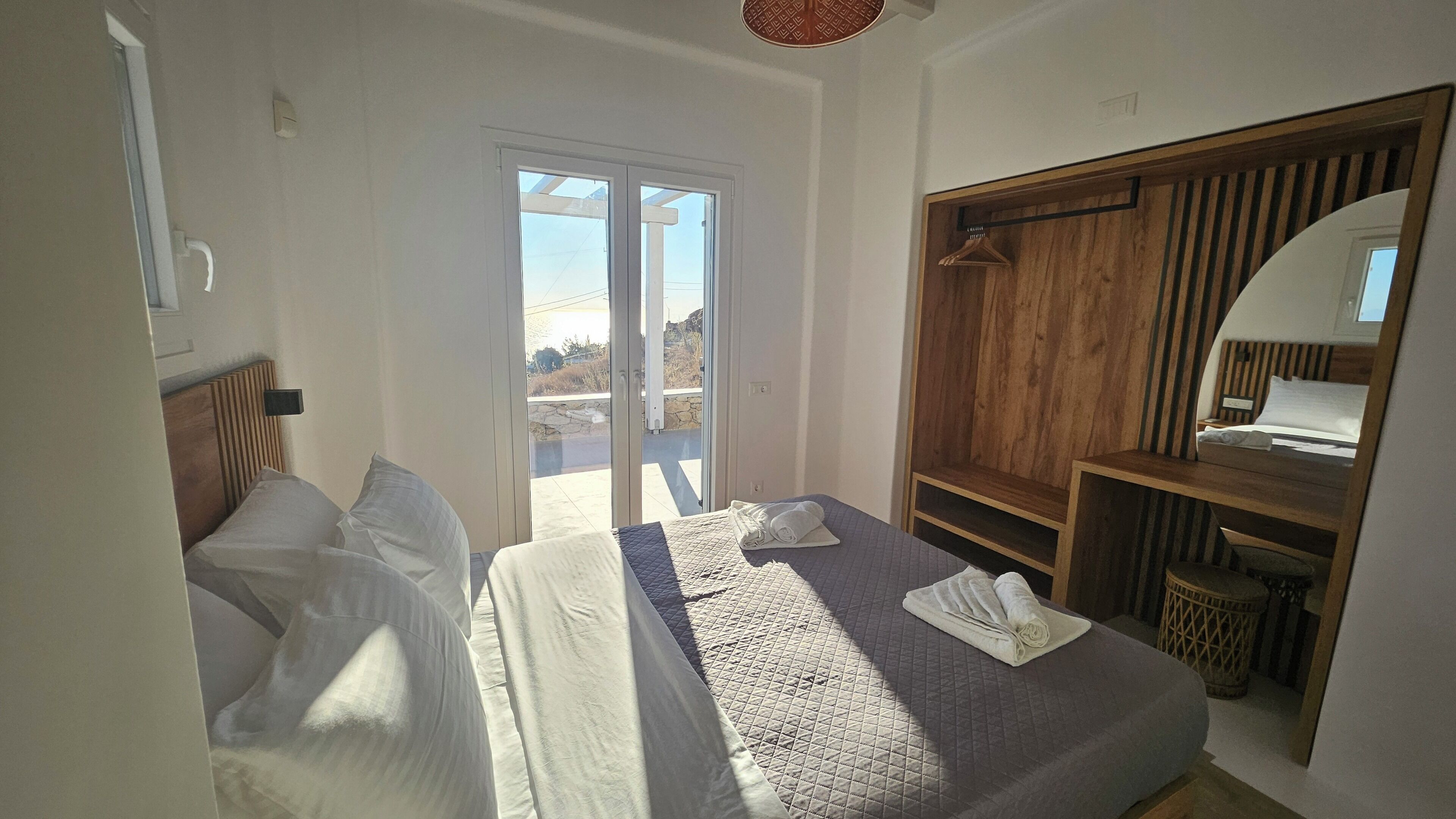 Ein Schlafzimmer mit einem Bett, einem Holzschrank, einem Spiegel und Blick durch eine Glastür.