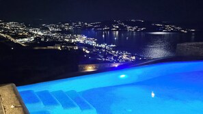 A nighttime view of a coastal town with a pool area. - Aether Mykonos 3BR Port View Villa (Tourlos)