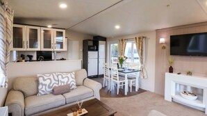 A modern living room with a sofa, coffee table, and dining area with chairs and a table. - Rosefinch Cabin (Scarborough)