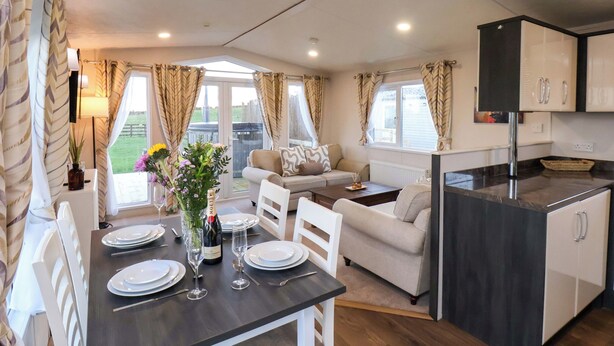 A cozy, well-lit room with a dining table set for two, a sofa, and a kitchen area with cabinets. - Rosefinch Cabin (Scarborough)