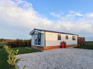 A single-story mobile home with a gravel driveway, a wooden fence, and a grassy area. - Rosefinch Cabin (Scarborough)