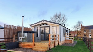 A single-story mobile home with a deck, a barbecue grill, and a fenced yard. - Rosefinch Cabin (Scarborough)