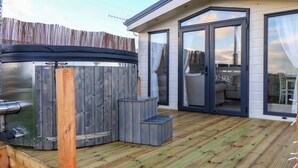 A modern outdoor deck with a hot tub, a wooden fence, and a building with large glass doors. - Rosefinch Cabin (Scarborough)