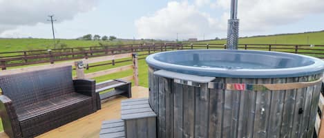 A hot tub with a wooden deck, a bench, and a wooden fence.