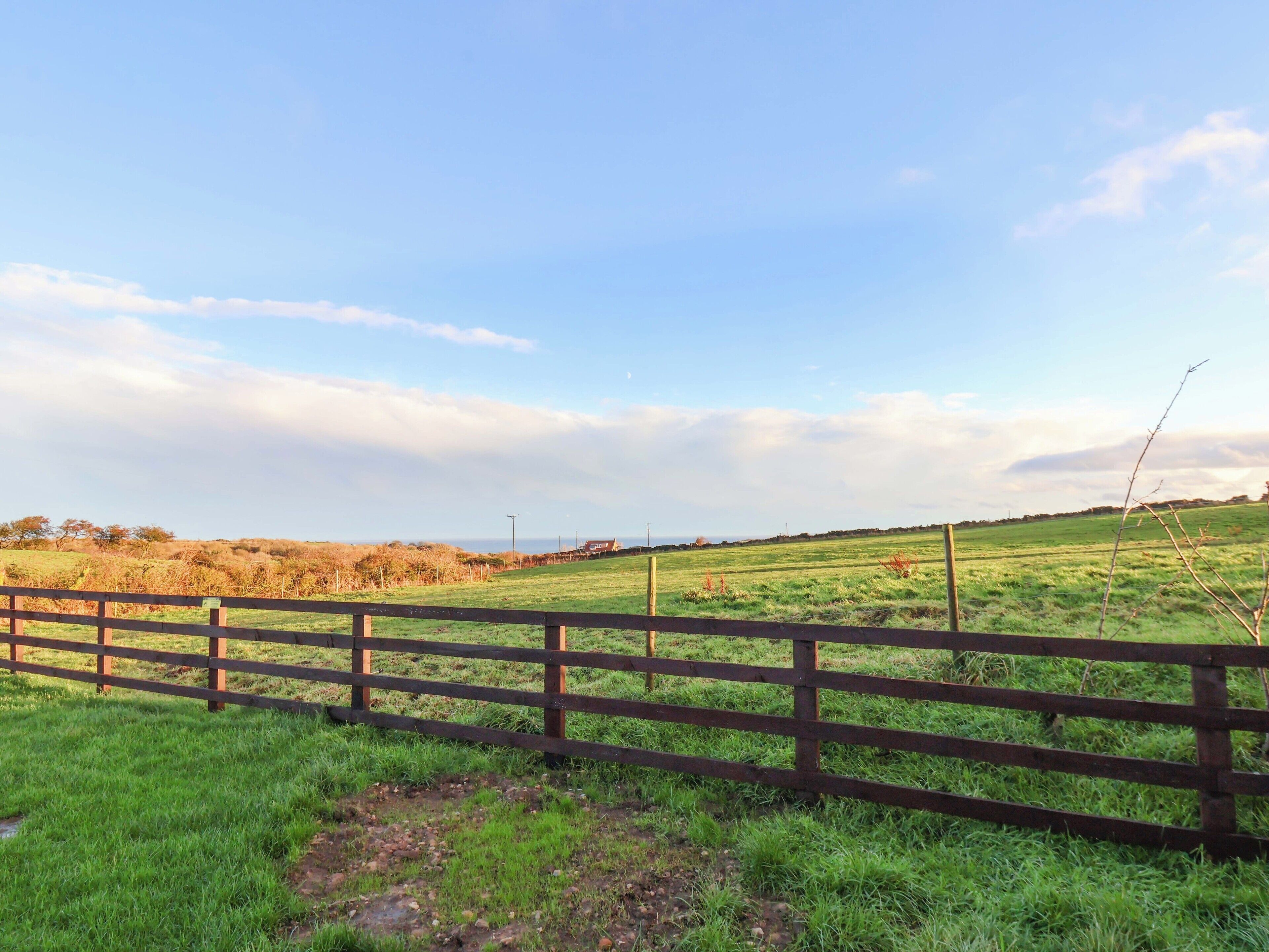 A rural landscape with a wooden fence, green fields, and a clear sky.