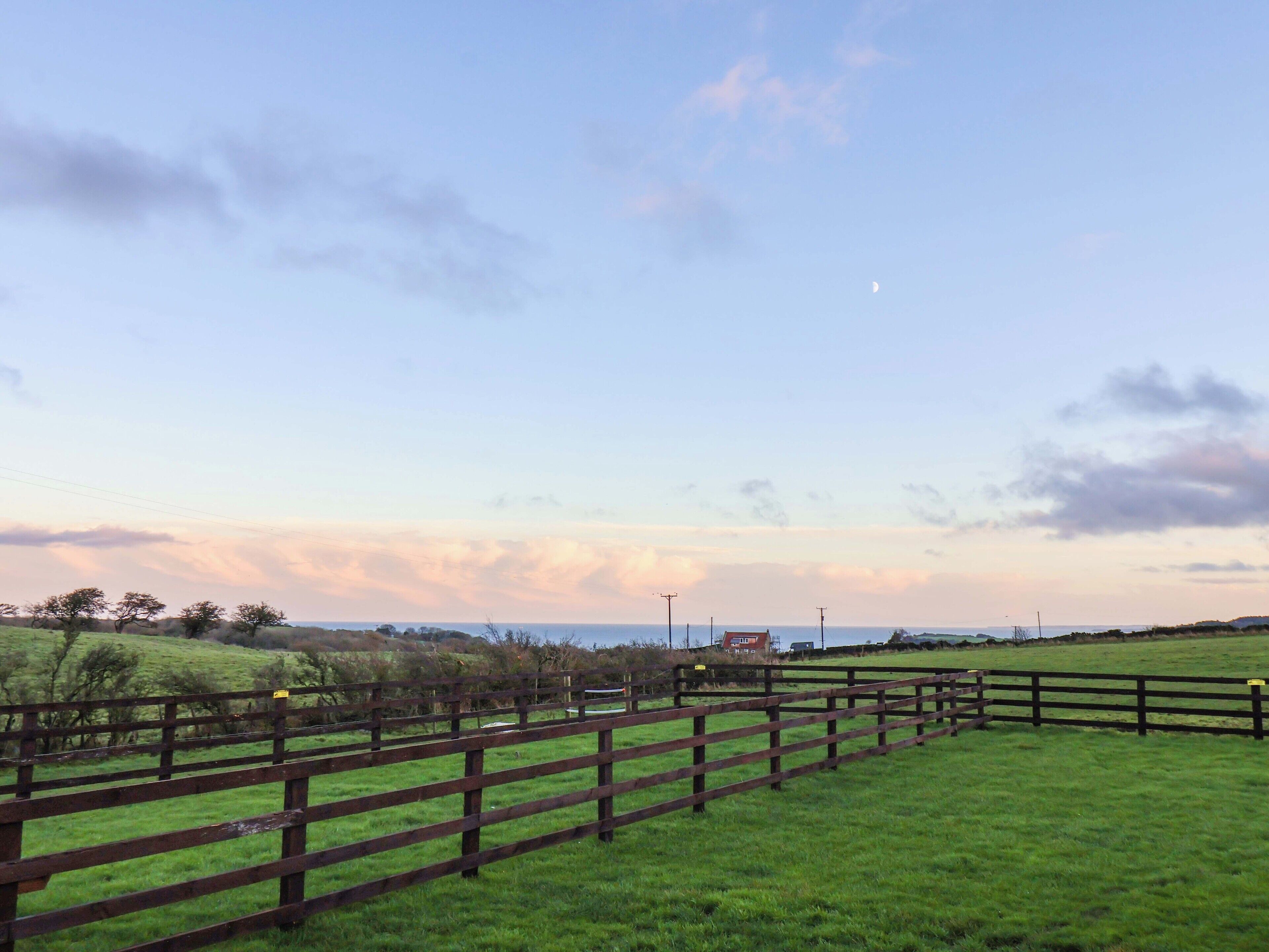 A rural landscape with a wooden fence, green fields, and a distant building.