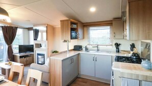Een compacte keuken met een fornuis, spoelbak en kastjes, een eethoek met een tafel en stoelen, en een televisie in een aparte kamer.
