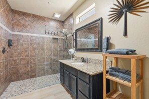 A bathroom with a shower, vanity, and a wooden shelf with towels.