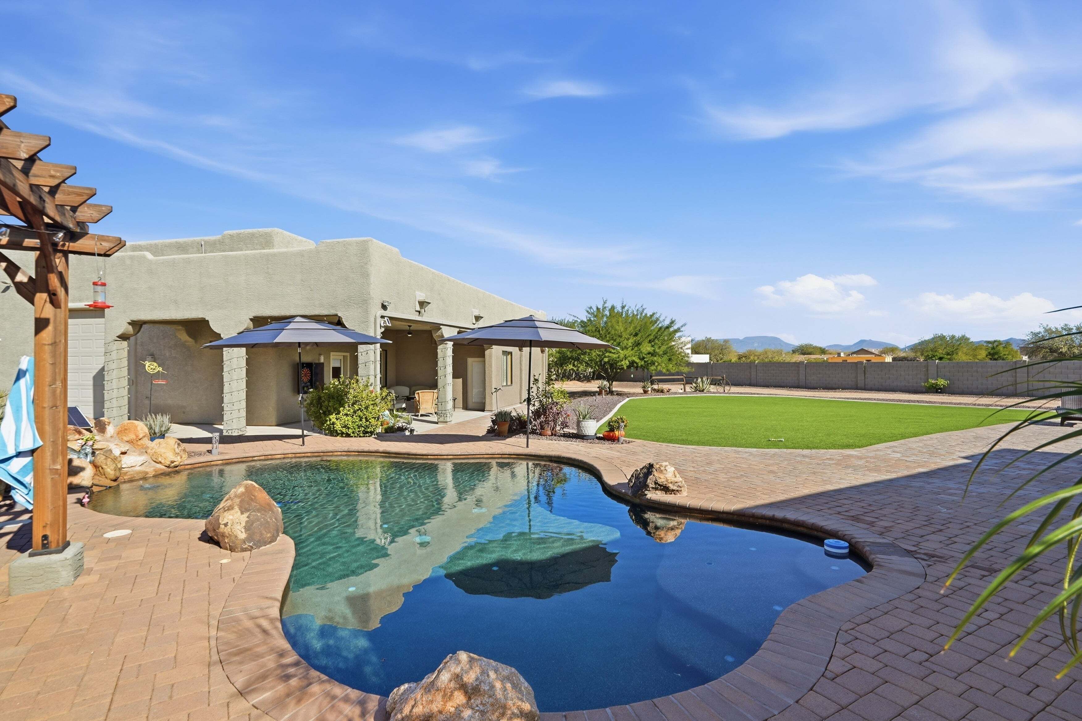 Un patio trasero con piscina, mobiliario de jardín y una pérgola.