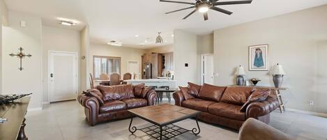 A spacious living room with leather sofas, a coffee table, and a ceiling fan.