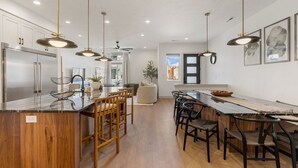 A modern kitchen with a central island, wooden chairs, and pendant lighting. - The Fish Bowl 6 Bedroom Townhouse (St. George)