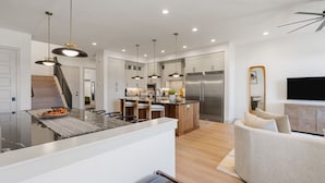 A modern kitchen with a central island, stainless steel appliances, and pendant lighting. - The Fish Bowl 6 Bedroom Townhouse (St. George)