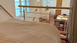 Een slaapkamer met een bed, een raam en uitzicht op een eetgedeelte met een tafel en stoelen.
