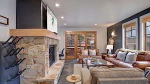 A cozy living room with a stone fireplace, leather sofas, a coffee table, and a stone wall. - Town Pointe A105 3 Bedroom Condo (Park City)