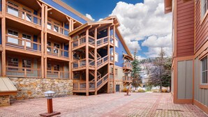 A multi-story building with a stone facade, wooden balconies, and a brick-paved courtyard. - Town Pointe A105 3 Bedroom Condo (Park City)