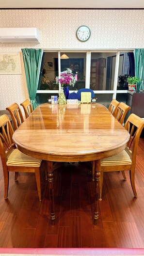 A round wooden dining table with six chairs, a clock on the wall, and a window with curtains. - Spacious family-friendly 4-bedroom house overlooking beautiful central Atami (Atami)