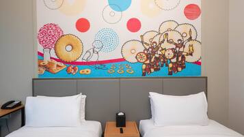 Ein Hotelzimmer mit zwei Betten, einem Nachttisch mit Telefon und Taschentuchbox sowie einem farbenfrohen Wandbild, das Donuts, eine Person und eine Szene aus der Kultur der amerikanischen Ureinwohner zeigt.