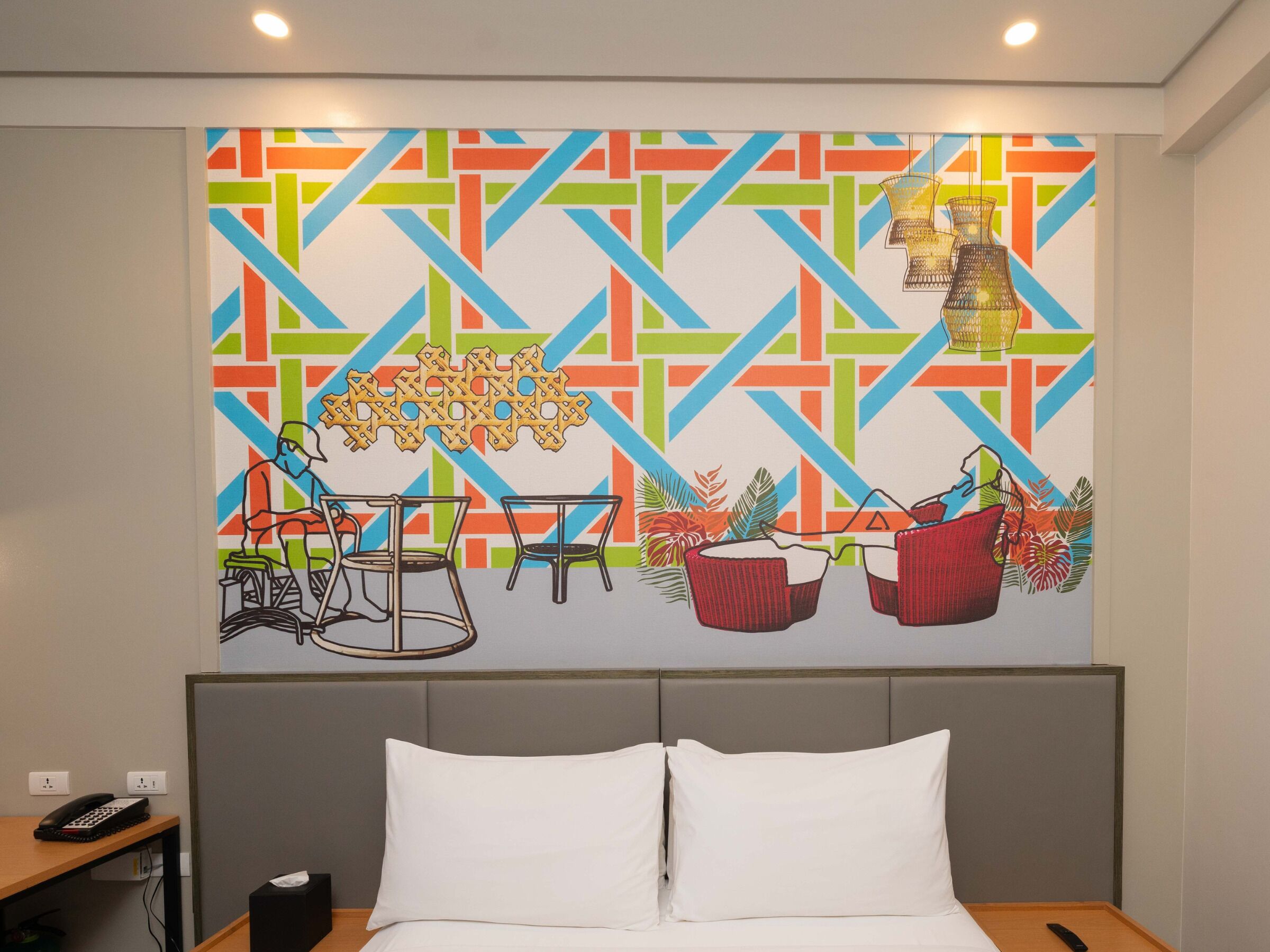 A hotel room with a bed, a desk with a phone, and a colorful abstract wall art.