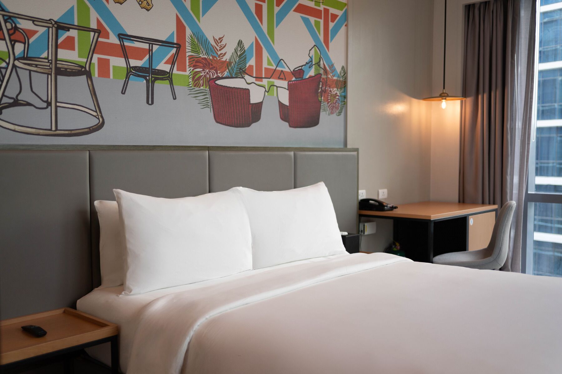 Una habitación de hotel con una cama grande, un escritorio, una silla y una obra de arte en la pared.